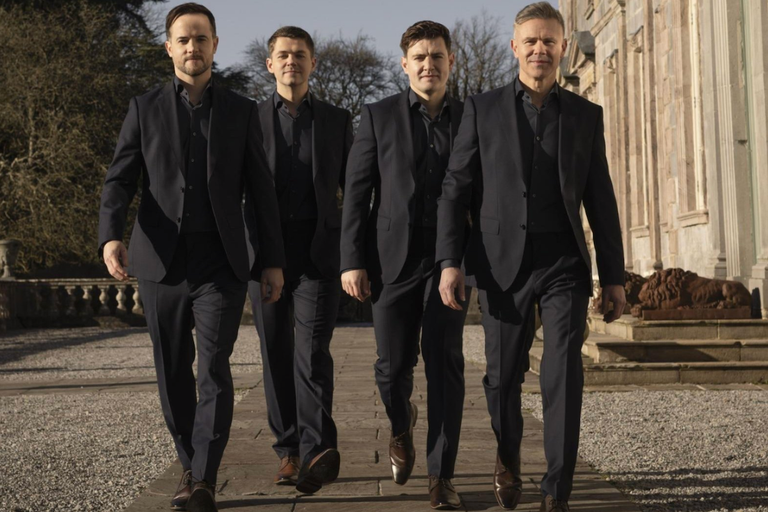 Irish singing group Celtic Thunder walking together outdoors in matching dark suits outside a historic building.
